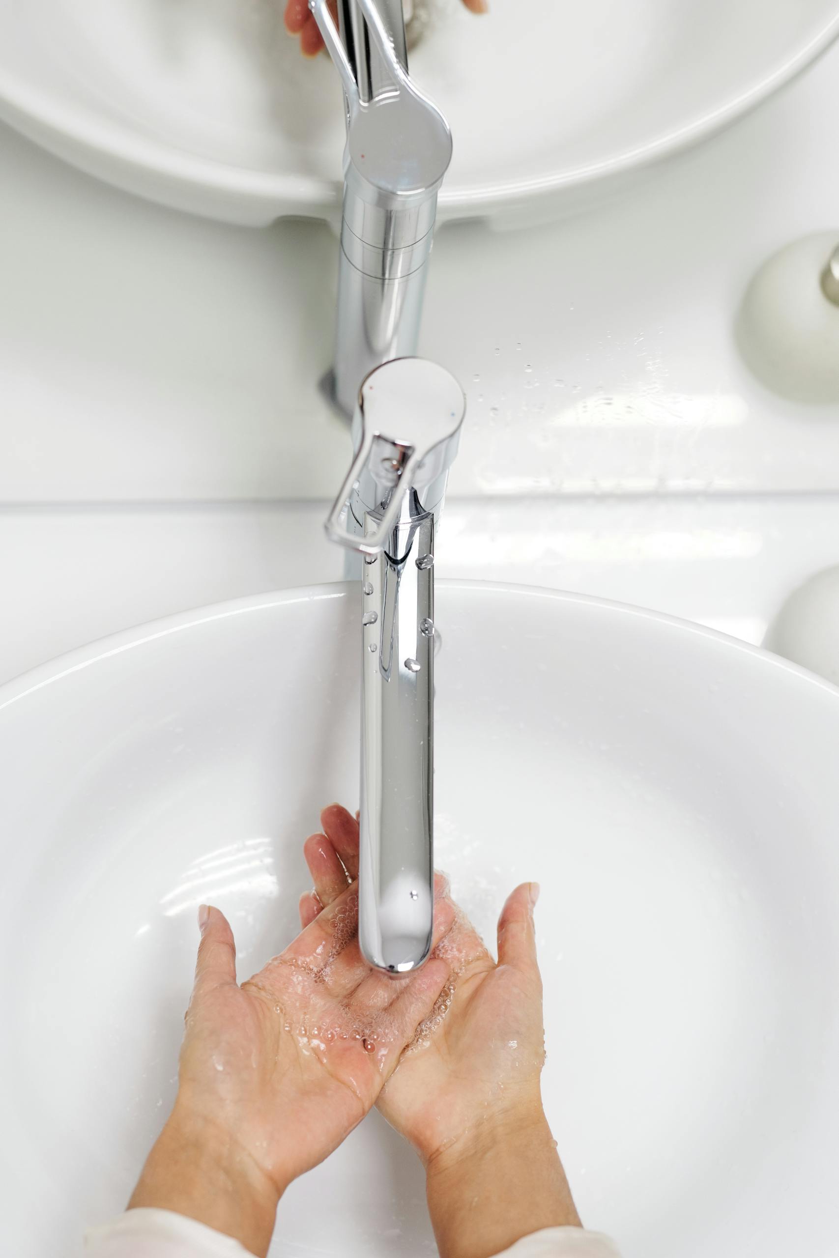 Hands washing under a sleek faucet with water flowing in a white basin