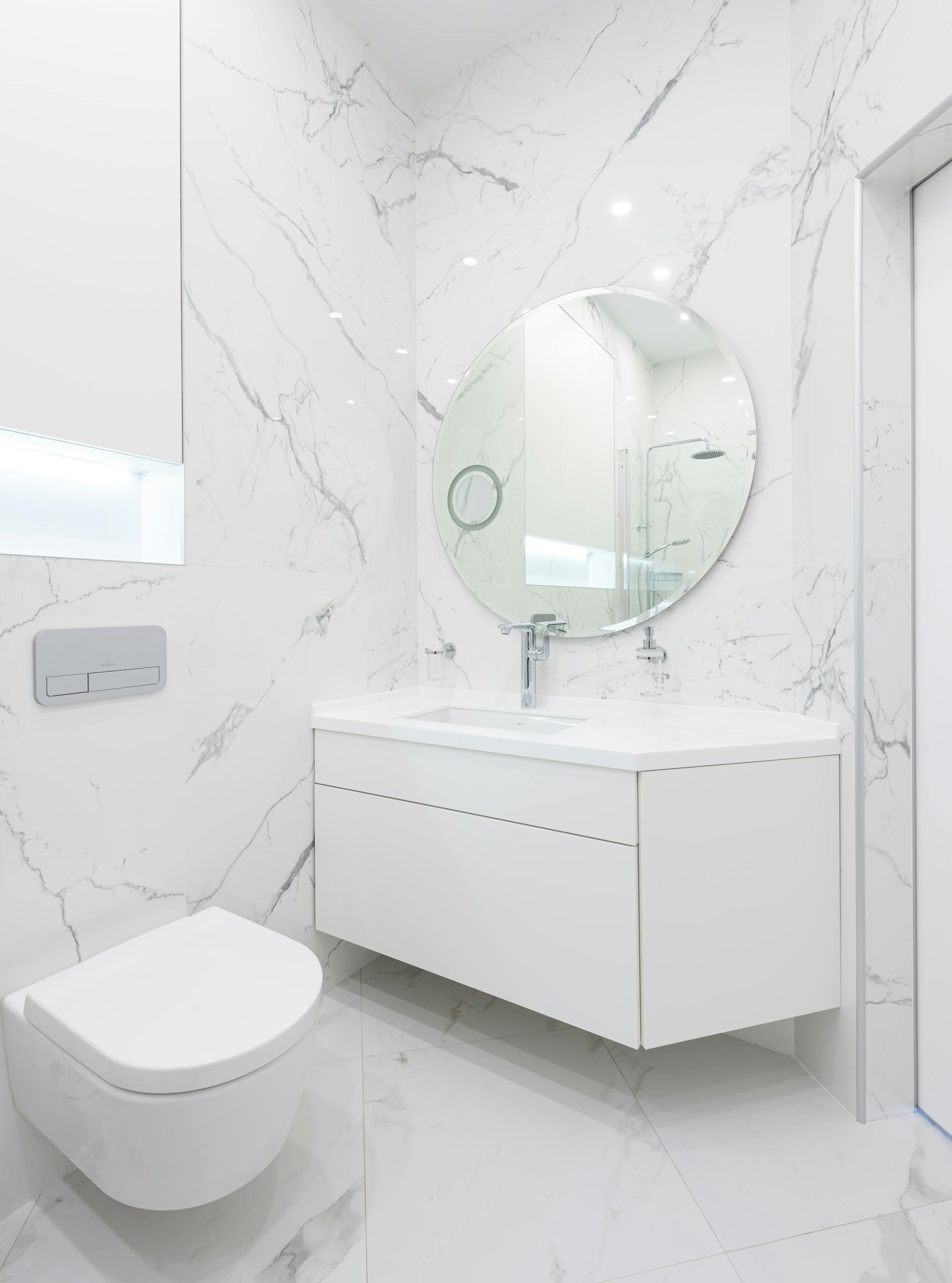 A sleek, minimal bathroom with white marble walls and round mirror.