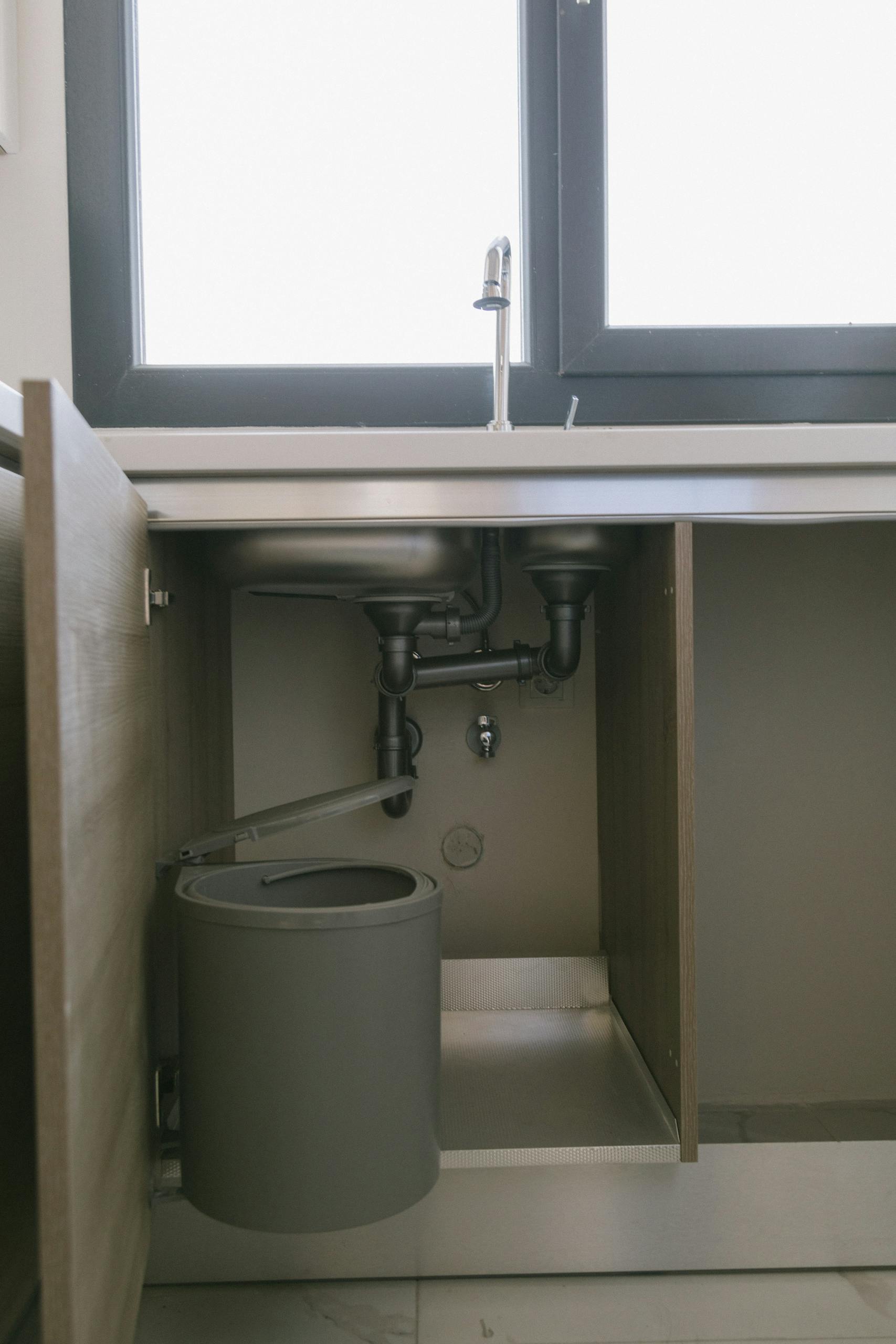 Under-sink view of modern plumbing with garbage bin in an Istanbul apartment kitchen.